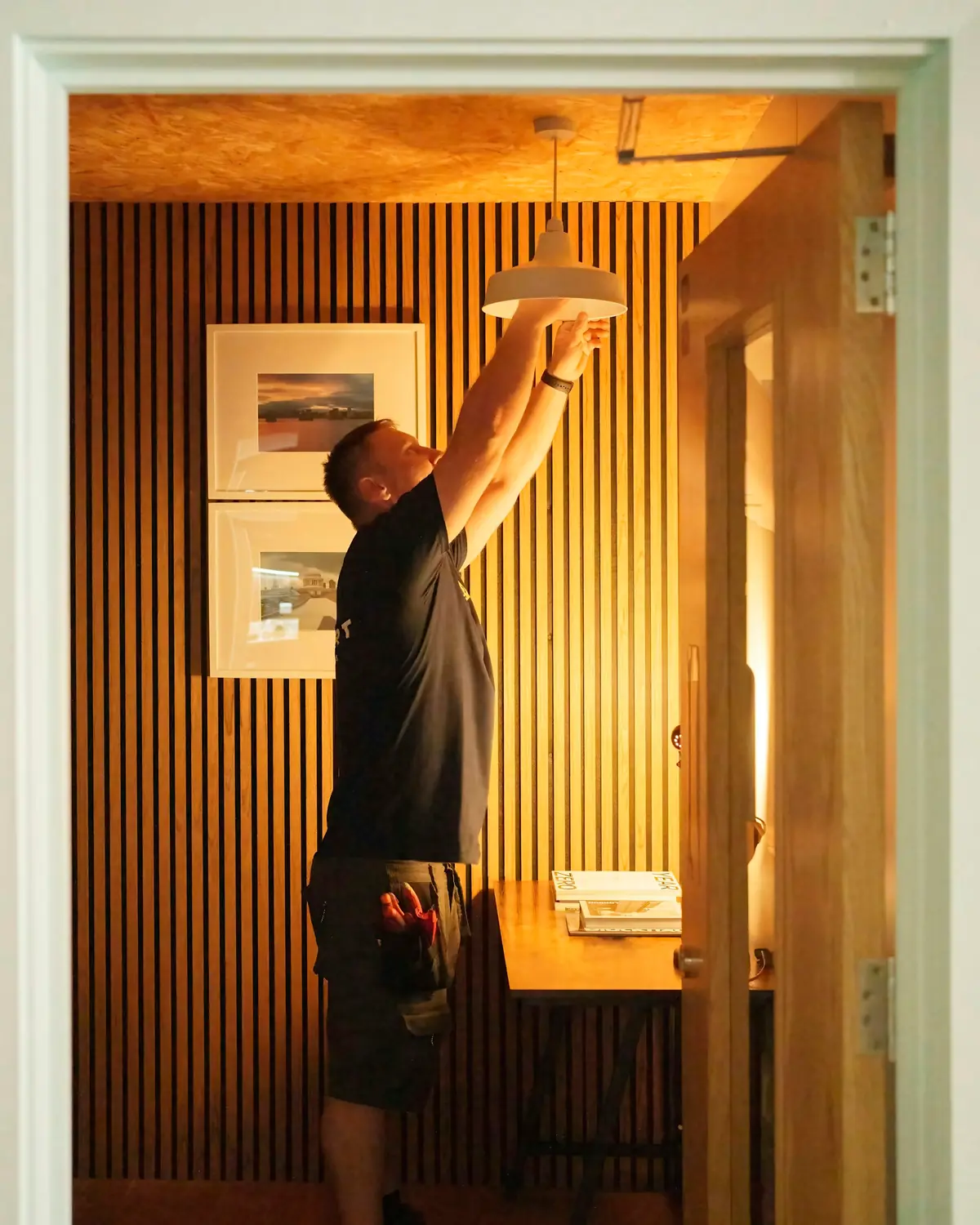 Man die een plafondlamp bevestigt in een kamer met houten lamellen
