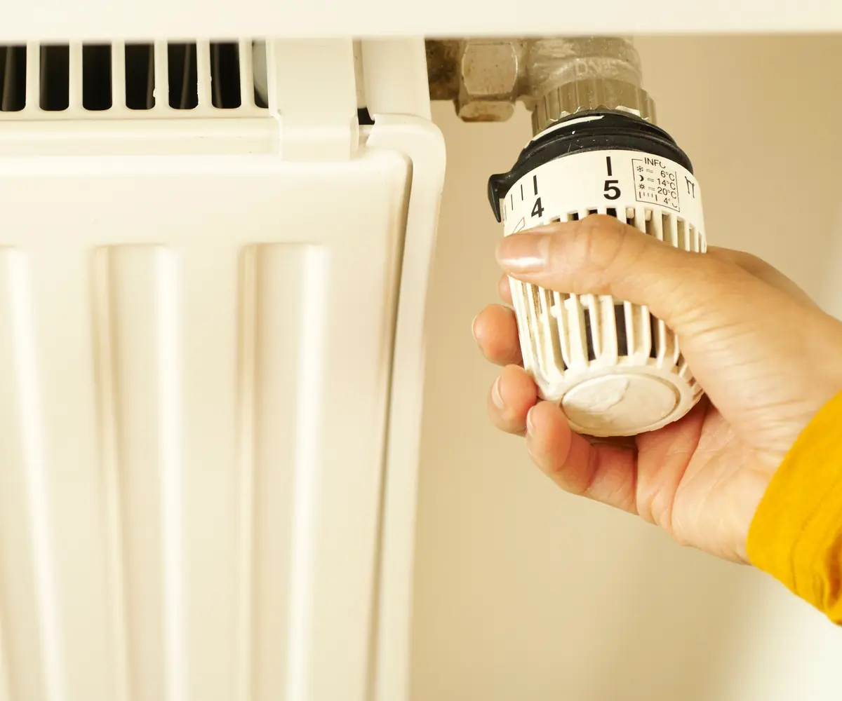 Hand draait aan de thermostaatknop van een witte radiator