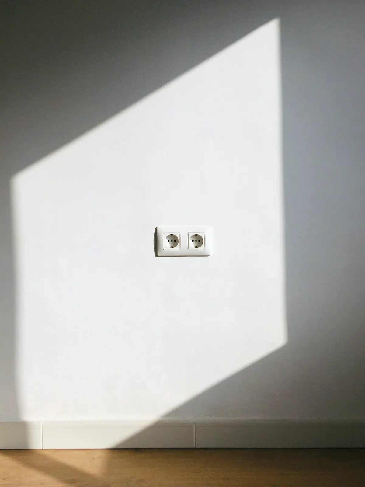 Dubbel stopcontact op een witte muur in het zonlicht
