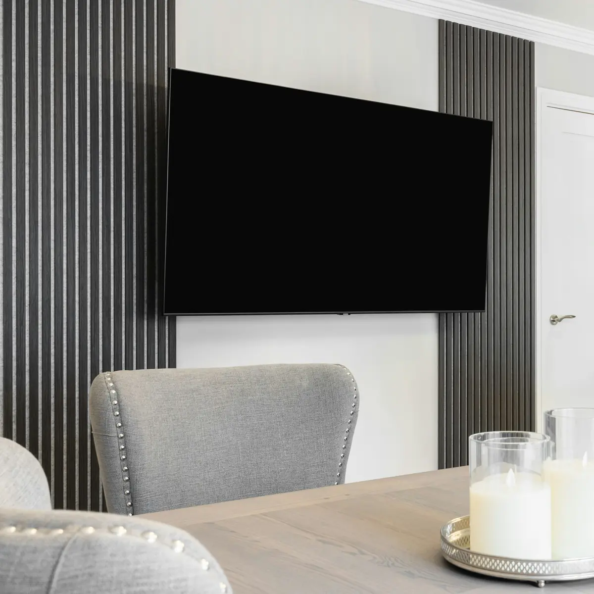 Televisie aan een wand met donkere lamellen boven een eettafel
