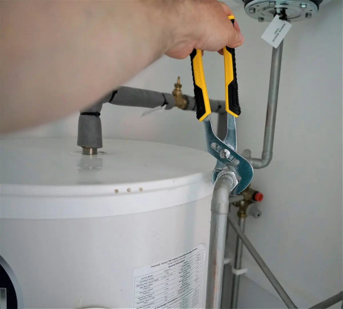 Hand met een waterpomptang aan een leiding op een boiler