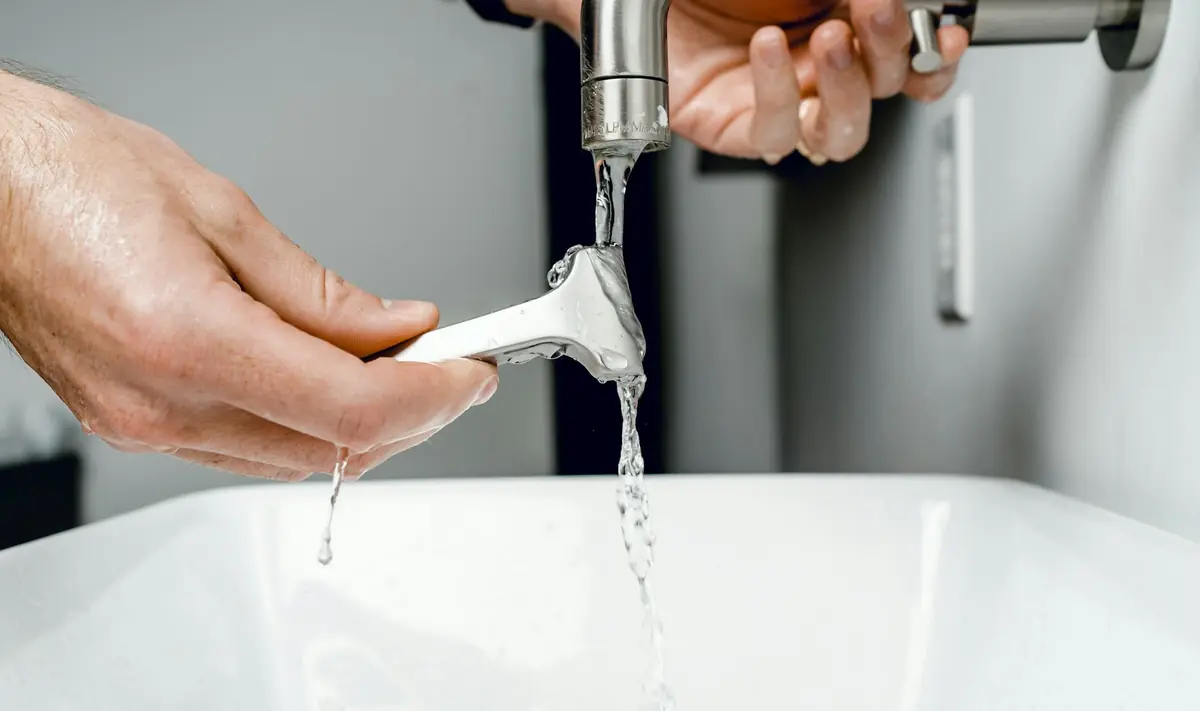 Handen met een steeksleutel aan een wastafelkraan waar water uit loopt